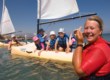 nanny laughing in the sea with young children on boat behind her in lakitira