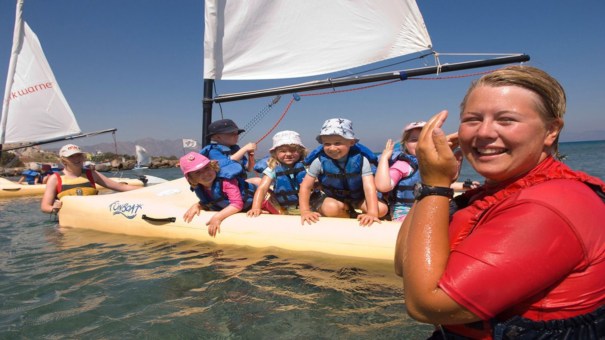 nanny laughing in the sea with young children on boat behind her in lakitira